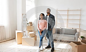 Happy millennial black couple standing in their new house among cardboard boxes on moving day