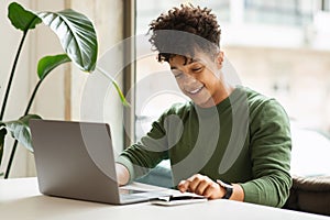 Happy millennial black man using gadgets at cafe