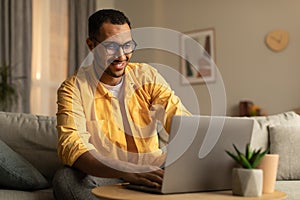Happy millennial black man using laptop, working or studying online, having online business conference at home office
