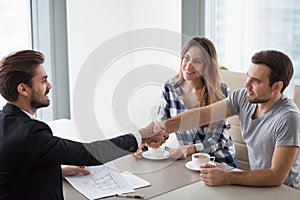 Happy millennial couple and realtor shake hands making property deal