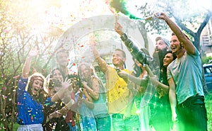 Happy millennial friends having fun at garden party with multicolored smoke bombs outside - Young millenial students celebrating