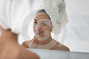 Happy millennial girl applying make up at mirror after shower