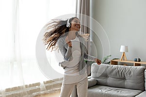Happy millennial girl in headphones dancing in living room