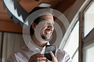 Happy millennial guy using smartphone, holding cell
