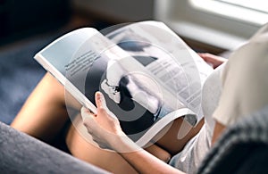Happy millennial lady reading fashion magazine with latest beauty trends or celebrity news and interview articles. photo