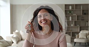 Happy millennial latin female homeowner showing keys to camera.