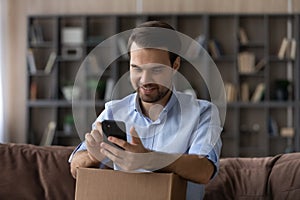 Happy millennial male shopper using mobile phone to shoot unpacking