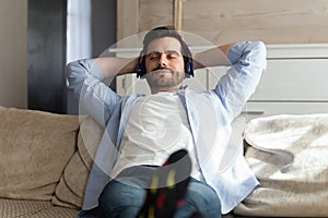 Happy millennial man resting on sofa listening to favorite music