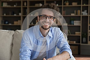 Happy millennial man sits on sofa posing, staring at camera