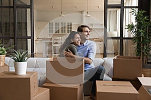 Happy millennial married couple hug on sofa at relocation day