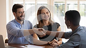 Happy millennial married couple shaking hands with financial advisor.