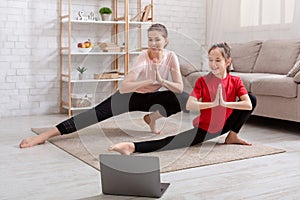 Happy millennial mother and her teenage daughter watching online sports video tutorial, doing exercises on floor at home