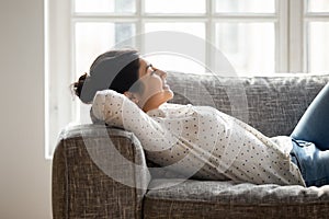 Happy millennial tranquil indian woman lying on comfortable couch.
