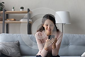 Happy millennial woman browsing internet on cellphone at home photo