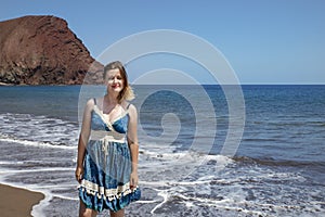 Happy millennial woman wearing a blue paisley dress while enjoying a beautiful day on La Tejita beach, Tenerife, Canary Islands photo