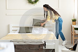 Happy millennial young woman making bed after wake up