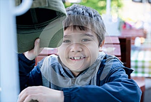 Happy mixed race boy holding cap hat and looking at camera with smiling face, Smile young kid waiting for lunch at outdoor cafe