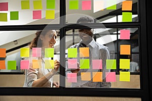 Happy mixed race colleagues standing near window glass board.