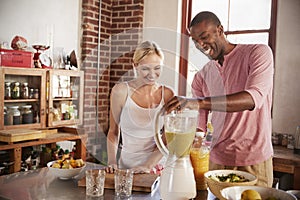 Happy mixed race couple making smoothies, using blender