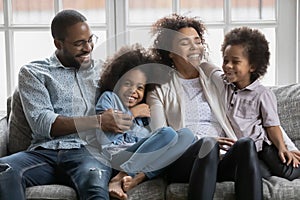 Happy mixed race couple parents relaxing on sofa with children.