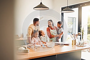 A happy mixed race family of five relaxing in the kitchen and cooking together. Loving black family being playful while