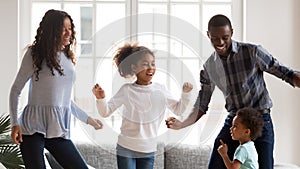 Happy mixed race family have fun dancing together at home