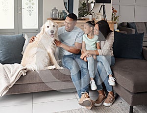 A happy mixed race family of three relaxing on the sofa with their dog. Loving black family being affectionate with a