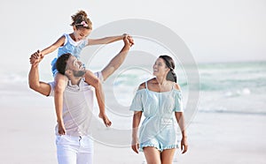 Happy mixed race family walking along the beach enjoying vacation. Adorable little sitting on her fathers shoulders