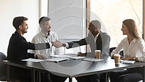 Happy mixed race millennial company representatives shaking hands with partners.