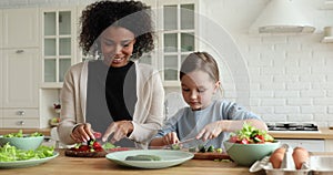 Happy mixed-race mom and child daughter cooking looking at camera