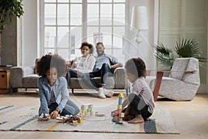 Happy mixed race parents watching small children playing toys.