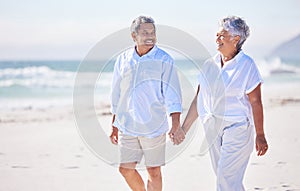 Happy mixed race senior couple holding hands while walking on the beach together. Mature couple traveling and enjoying