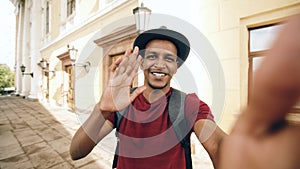 Happy mixed race tourist man having online video chat using his smartphone camera standing near historical building in
