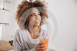 Happy mixed race woman holding orange juice and looking to camera.