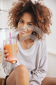 Happy mixed race woman holding orange juice and looking to camera.