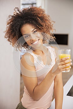 Happy mixed race woman holding orange juice and looking to camera.