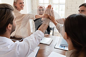 Happy mixed race young and older colleagues giving high five.