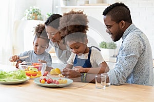 Happy mixed race young parents teaching little kids cooking.