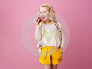 Happy modern child isolated on pink eating an apple