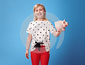 Happy modern child showing piggy bank with plaster on blue