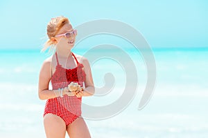 Happy modern girl with seashell looking into distance on beach