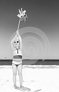 Happy modern girl on seashore holding windmill toy