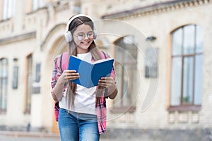 Happy modern kid read book listening to audio language course in headphones outdoors, English, copy space