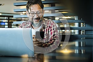 Happy modern mature man at work in coworking workplace alternative office using laptop computer and mobile phone to communicate.