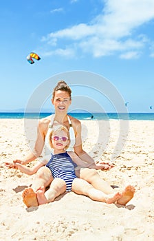 Happy modern mother and child in beachwear sitting on seashore