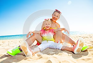 Happy modern mother and daughter sitting on seacoast