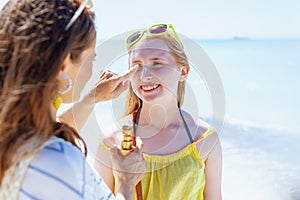 Happy modern mother and teenage daughter at beach applying spf
