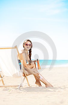 Happy woman applying sun block while sitting in beach chair