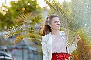 happy modern woman in pink dress and white jacket in city