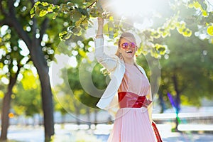 happy modern woman in pink dress and white jacket in city